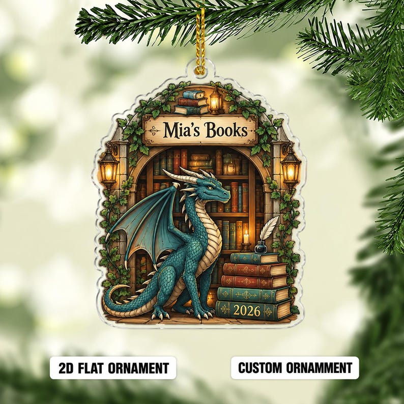 May include: A flat, arched acrylic ornament featuring a blue dragon sitting in a library with bookshelves, ivy, and lanterns. The text reads Mia's Books and 2026 on a stack of books. It includes a gold hanging cord for display on a tree branch.