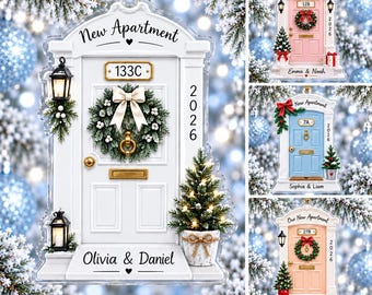 May include: A flat, decorative ornament shaped like a front door with the text New Apartment, 133C, 2026, and Olivia & Daniel. The white door features a green wreath with a white bow, two black lanterns, and a small potted Christmas tree.