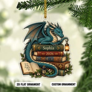 May include: A flat acrylic ornament featuring a teal dragon perched on a stack of books. The books are labeled with the name Sophia and the year 2026. An open book displays the text Good Books Brighter Days, accompanied by a small ink bottle.