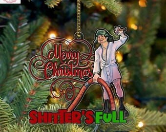 May include: A Christmas tree ornament with the words "Merry Christmas" in red script and "Shitter's Full" in green. The ornament features a cartoon image of a man in a bathrobe holding a hose. The ornament hangs from a gold string.