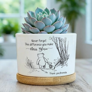 May include: A white ceramic planter with a succulent plant. The planter features a black and white illustration of Winnie the Pooh and Piglet, with the text "Never forget the difference you make Mrs. Gloria" and "Thank you, Brenda."