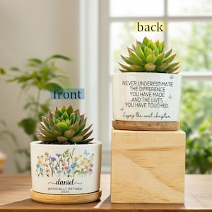 May include: Two white ceramic pots with succulents. One pot has a floral design and the name "daniel" with "OFFICIALLY RETIRED 2025". The other pot has the text "NEVER UNDERESTIMATE THE DIFFERENCE YOU HAVE MADE AND THE LIVES YOU HAVE TOUCHED. Enjoy the next chapter."