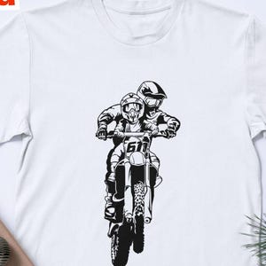 Peut inclure: T-shirt blanc avec un motif noir et blanc de deux personnes sur une moto. Le design comprend le numéro 61 sur la moto. Les mots "Digital Download" sont dans le coin supérieur gauche. Le coin inférieur gauche contient les mots "ART INVADER" et des icônes de type de fichier.