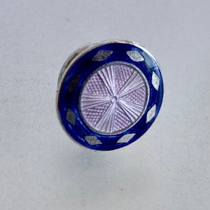 May include: A small, round, silver button with a blue enamel border and a white enamel design. The center of the button has a lavender enamel design with a raised, circular pattern.