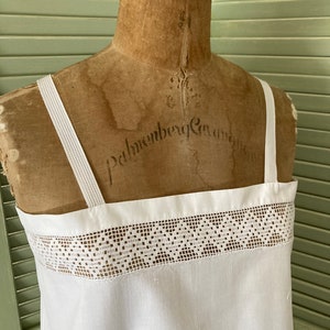 May include: White cotton slip with a lace trim. The slip is on a vintage dress form.