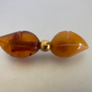 May include: A gold-toned pin with two amber leaf-shaped stones.