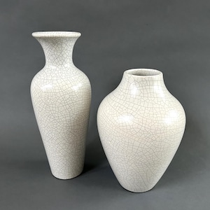 Könnte beinhalten: Zwei weiße Keramikvasen mit einer Craquelé-Glasur. Die Vase links ist höher und schmaler als die Vase rechts.