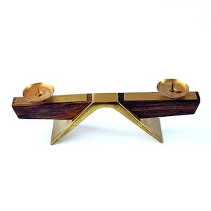 K&ouml;nnte beinhalten: Ein Kerzenhalter im Mid-Century-Modern-Stil. Der Kerzenhalter hat eine dunkle Holzbasis mit Messingakzenten und zwei Messingkerzenschalen. Die Basis wird von einem Messingbogen und einer Basis getragen, wodurch ein ausgewogenes und elegantes Design entsteht.