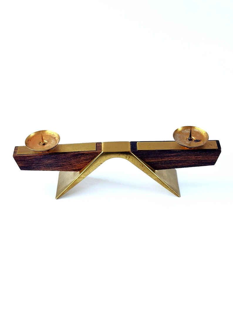 K&ouml;nnte beinhalten: Ein Kerzenhalter im Mid-Century-Modern-Stil. Der Kerzenhalter hat eine dunkle Holzbasis mit Messingakzenten und zwei Messingkerzenschalen. Die Basis wird von einem Messingbogen und einer Basis getragen, wodurch ein ausgewogenes und elegantes Design entsteht.