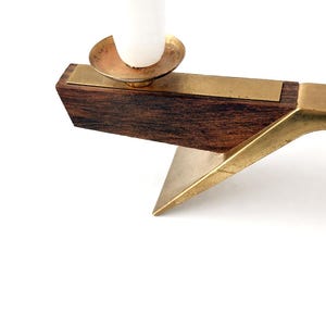 K&ouml;nnte beinhalten: Ein Kerzenhalter im Mid-Century-Stil mit einem dunklen Holzsockel und Messingakzenten. Der Kerzenhalter hat eine Messingkerzenschale und eine wei&szlig;e Kerze. Das Design ist geometrisch und minimalistisch.