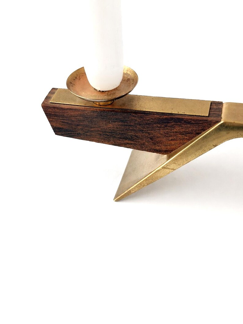 K&ouml;nnte beinhalten: Ein Kerzenhalter im Mid-Century-Stil mit einem dunklen Holzsockel und Messingakzenten. Der Kerzenhalter hat eine Messingkerzenschale und eine wei&szlig;e Kerze. Das Design ist geometrisch und minimalistisch.