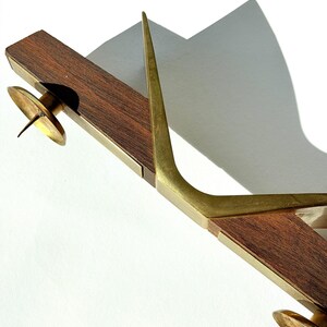 K&ouml;nnte beinhalten: Ein Vintage-Kerzenhalter mit Holzsockel und Messingdetails. Der Kerzenhalter hat zwei Messing-Kerzenschalen und ein hohes, gebogenes Messingelement. Das Holz ist dunkelbraun und das Messing hat einen warmen, goldenen Farbton.