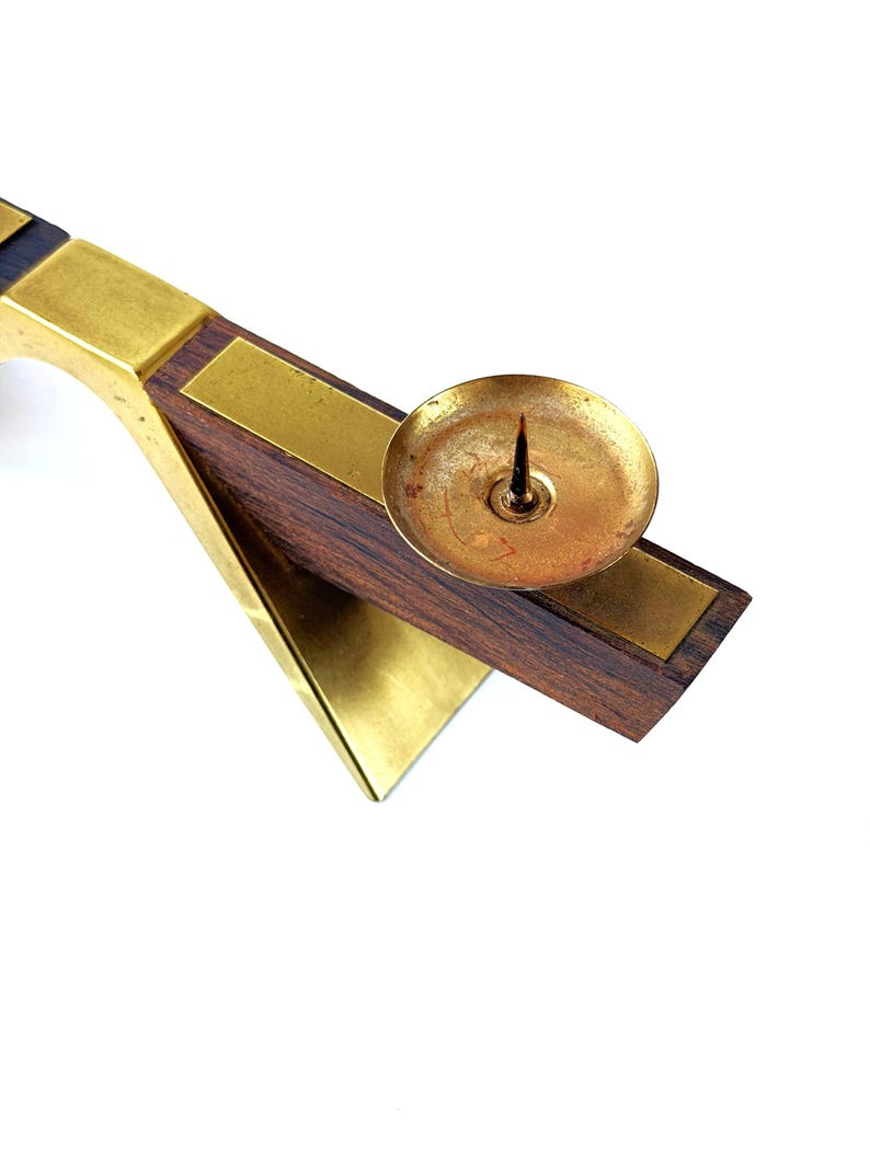 K&ouml;nnte beinhalten: Ein Vintage-Kerzenhalter mit einer Messing-Tasse und einem Dorn, der auf einem dunklen Holzsockel mit Messingakzenten steht. Der Halter hat ein geometrisches Design mit einem dreieckigen Sockel und einem rechteckigen Arm.