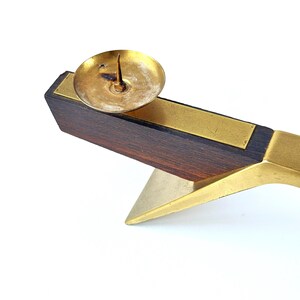 K&ouml;nnte beinhalten: Ein Vintage-Kerzenhalter mit dunklem Holzsockel, Messingakzenten und einer kleinen Messingkerzenschale. Der Halter hat ein geometrisches Design. Der Artikel ist vor einem wei&szlig;en Hintergrund platziert. Ein klassischer Einrichtungsgegenstand.