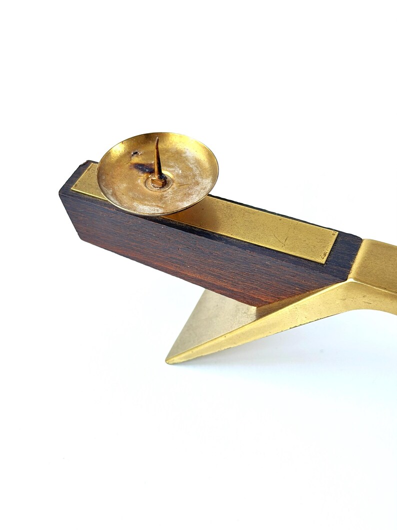 K&ouml;nnte beinhalten: Ein Vintage-Kerzenhalter mit dunklem Holzsockel, Messingakzenten und einer kleinen Messingkerzenschale. Der Halter hat ein geometrisches Design. Der Artikel ist vor einem wei&szlig;en Hintergrund platziert. Ein klassischer Einrichtungsgegenstand.