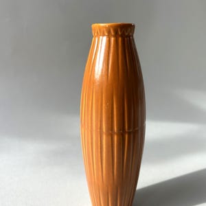 Könnte beinhalten: Eine braune Keramikvase mit geripptem Design. Die Vase ist hoch und schmal, mit einem abgerundeten Boden und einem leicht ausgestellten oberen Rand.