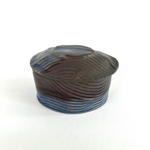 Peut inclure: Petit récipient en céramique avec couvercle. Le récipient est brun foncé avec des lignes horizontales en forme de vagues. La partie inférieure est bleue. Le couvercle présente un motif de vagues similaire et est d'une nuance de brun plus foncée.
