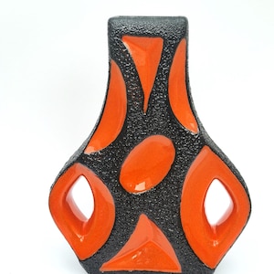 Puede incluir: Un jarrón decorativo con exterior negro texturizado y formas geométricas naranja vibrantes. El jarrón presenta un diseño único con cortes abiertos y un acabado brillante, ideal para la decoración del hogar.