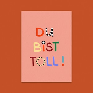 Könnte beinhalten: Eine rosa Karte mit dem deutschen Satz "Du bist toll!" in bunten, verspielten Buchstaben. Die Wörter sind in verschiedenen Farben, darunter Rot, Gelb, Grün und Blau, mit dekorativen Mustern.