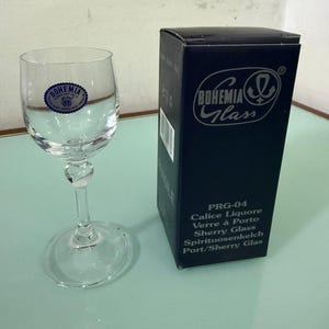 Könnte beinhalten: Ein klares Bohemia-Likörglas mit rundem Fuß und dekorativem Stiel, neben einer dunkelblauen Schachtel mit dem Bohemia Glass-Logo und Produktinformationen. Auf der Schachtel steht "Sherry Glass".