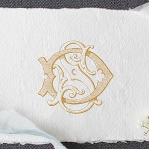 Könnte beinhalten: Ein goldfarbenes Monogramm mit den Buchstaben "S" und "D", die in einer dekorativen, stilisierten Schriftart miteinander verschlungen sind.