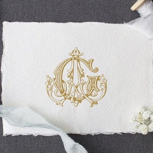 May include: A gold monogram featuring the letters "C" and "G" intertwined, surrounded by decorative flourishes. The monogram is printed on a white piece of paper.