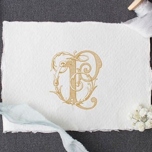 May include: A gold-colored monogram with the letters "T" and "P" intertwined in a decorative floral design. The monogram is printed on a white piece of paper.