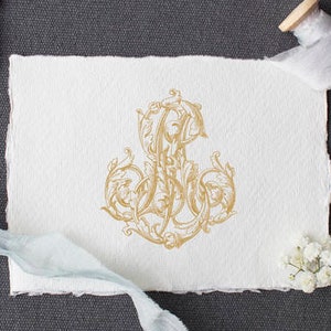 Puede incluir: Un monograma dorado con un diseño floral decorativo sobre un fondo de papel blanco. El monograma está rodeado de una cinta azul y un carrete de cinta.