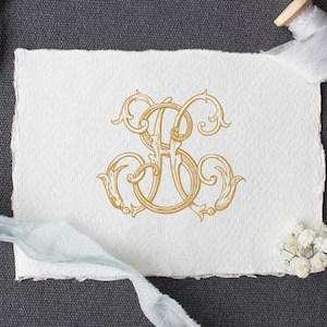 Puede incluir: Un monograma dorado con las letras "HS" entrelazadas en una fuente de letra decorativa. El monograma está en un trozo de papel blanco con un borde deshilachado. El papel está sobre una superficie gris con un par de tijeras, un carrete de cinta blanca y una ramita de flores blancas.