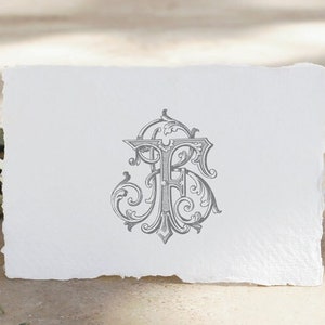 Puede incluir: Una tarjeta blanca con un monograma gris, adornado y decorativo de las letras "F" y "R" en una fuente de escritura. La tarjeta está sobre una superficie marrón claro con una rama de olivo verde.