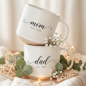 May include: A white ceramic mug with a black handle and the text "But First, Coffee" in a handwritten style. The mug is on a white surface. The mug is 10 cm tall.