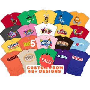 May include: A collection of various coloured t-shirts featuring different candy and snack brand logos and character graphics. A central red starburst shape contains the text SALE! and the text CUSTOM FROM 48+ DESIGNS in orange letters.