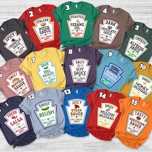 May include: A collection of fifteen short-sleeved t-shirts in various colors, each featuring a graphic print shaped like a condiment bottle label. The designs include text labels such as Spicy Chipotle Sauce, Italian Pizza Sauce, Toasted Sesame Oil, Dark Chocolate Sauce, Cheesy Alfredo Sauce, Sweet Buffalo Sauce, Sour Dill Pickles, Salty Soy Sauce, Cool Original Ranch Dressing, Sweet Honey Mustard, Fresh Salsa, Sweet Relish, Juicy Steak Sauce, Spicy Yellow Mustard, and Tasty Szechuan Sauce.