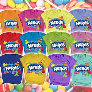 Può includere: Una collezione di dodici magliette a maniche corte in vari colori a tinta unita, ognuna con il logo delle caramelle Nerds in testo bianco su una grafica blu, circondato da piccole illustrazioni colorate di personaggi dei cartoni.