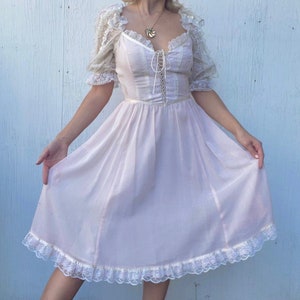 May include: A vintage-style, light pink dress with a lace bodice and a lace trim around the hem. The dress has a fitted bodice and a flowing skirt.