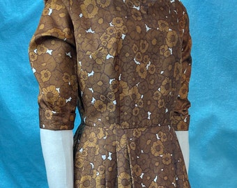May include: A brown dress with a white floral print. The dress has a scoop neck and 3/4 sleeves. The dress is fitted at the waist and flares out to a full skirt.