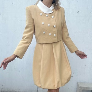 May include: A yellow vintage skirt suit with a double-breasted jacket and white buttons. The skirt is a-line and has a bubble hem.
