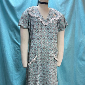 May include: A vintage teal blue and white patterned dress with a white lace trim around the neckline and pockets. The dress has short sleeves and a v-neck.