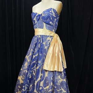 May include: A strapless blue and white patterned dress with a large yellow satin bow at the waist.