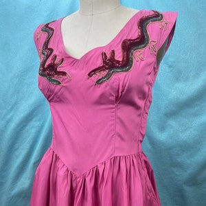 May include: A pink dress with a sweetheart neckline and short sleeves. The dress is decorated with a beaded design of a dragon on the bodice.