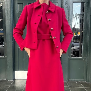 May include: A vibrant crimson dress and matching jacket set. The dress has a fitted bodice and a slightly flared skirt. The jacket has a collar and button closure. Both pieces feature decorative buttons.