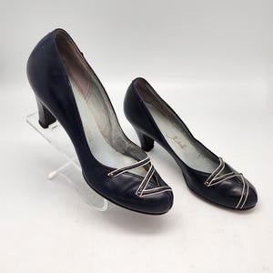 May include: A pair of navy blue leather heeled shoes with gold accents. The shoes have a criss-cross strap design and a rounded toe.
