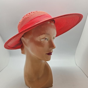 May include: A vibrant red sun hat with a wide brim, displayed on a mannequin head. The hat features a woven crown and a matching red ribbon band. The brim is a generous size, offering ample sun protection. The hat is a stylish accessory.