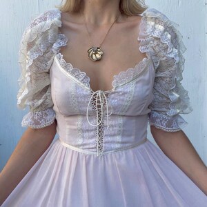 May include: A light pink dress with a lace bodice and ruffled sleeves. The dress has a lace-up detail in the front and a full skirt.
