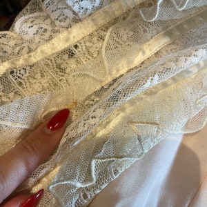 May include: Close-up of a white lace trim with a satin ribbon. The lace has a delicate floral pattern and is layered with ruffles.