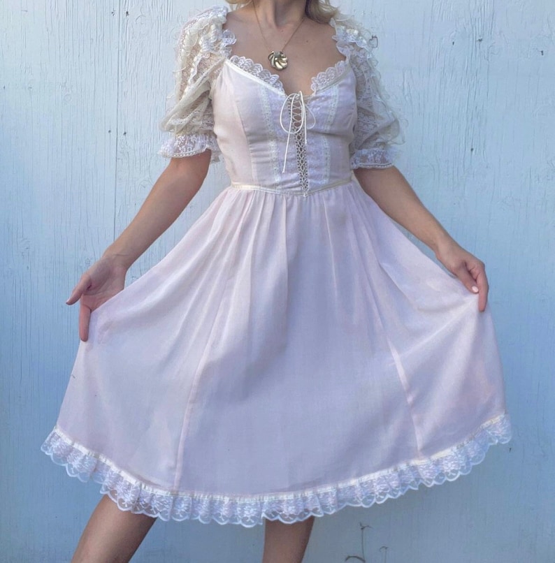May include: A vintage-style, light pink dress with a lace bodice and a lace trim around the hem. The dress has a fitted bodice and a flowing skirt.
