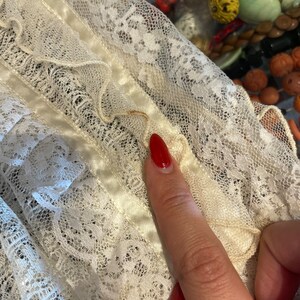 May include: White lace fabric with a satin ribbon trim. The lace has a delicate floral pattern.