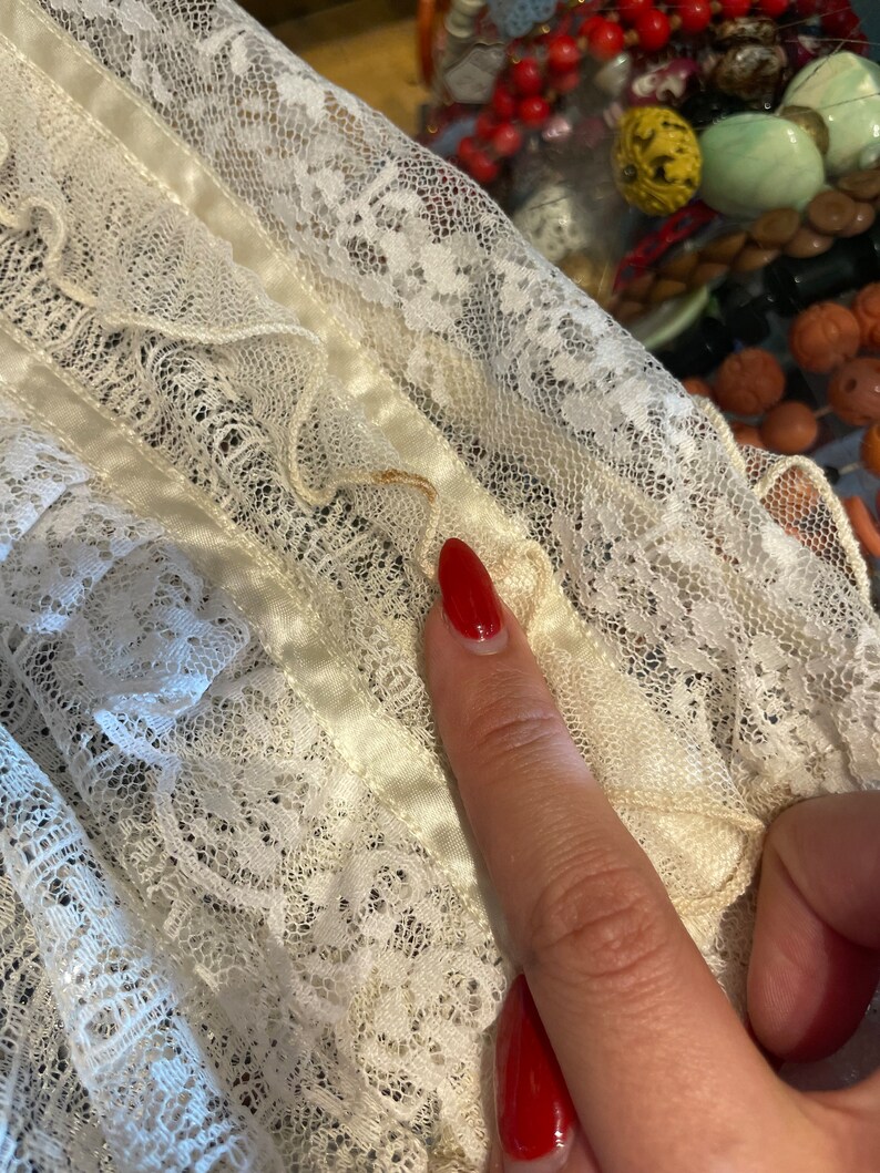 May include: White lace fabric with a satin ribbon trim. The lace has a delicate floral pattern.