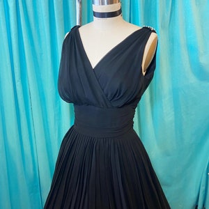 May include: A black sleeveless dress with a V-neckline and a pleated skirt. The dress is made of a soft, flowing fabric.