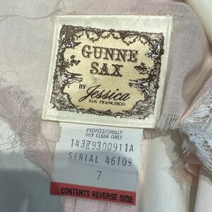 May include: A white tag with brown text that reads "GUNNE SAX by Jessica SAN FRANCISCO". Below the text is a smaller white tag with brown text that reads "PROFESSIONALLY DRY CLEAN ONLY 1439300911A SERIAL 46109 7 CONTENTS REVERSE SIDE".